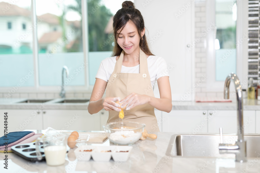 A young asian lady crack an egg into the bowl filled with flour, ready to mix for cake batter A young asian lady crack an egg into the bowl filled with flour, ready to mix for cake batter