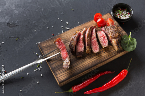 Rib eye steaks and spices on wood at black background