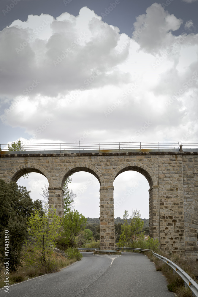Naklejka premium Road passing through the eyes of an old stone bridge for the railway 