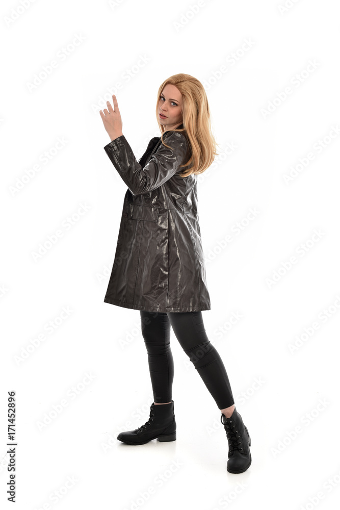 full length portrait of girl wearing black clothes with long leather jacket. standing pose on white background.