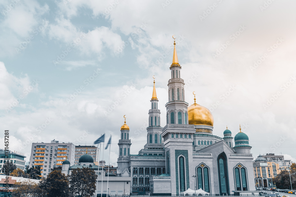 Frontal view of The Grand Cathedral Mosque: bright golden domes and spires with crescents, ornamental facade, residential houses around, parking  with cars in foreground, Moscow, Russia