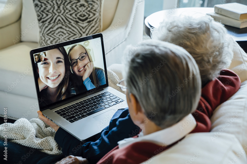 Senior couple video conferencing with granddaughters through laptop computer at home Senior couple video conferencing with granddaughters through laptop computer at home