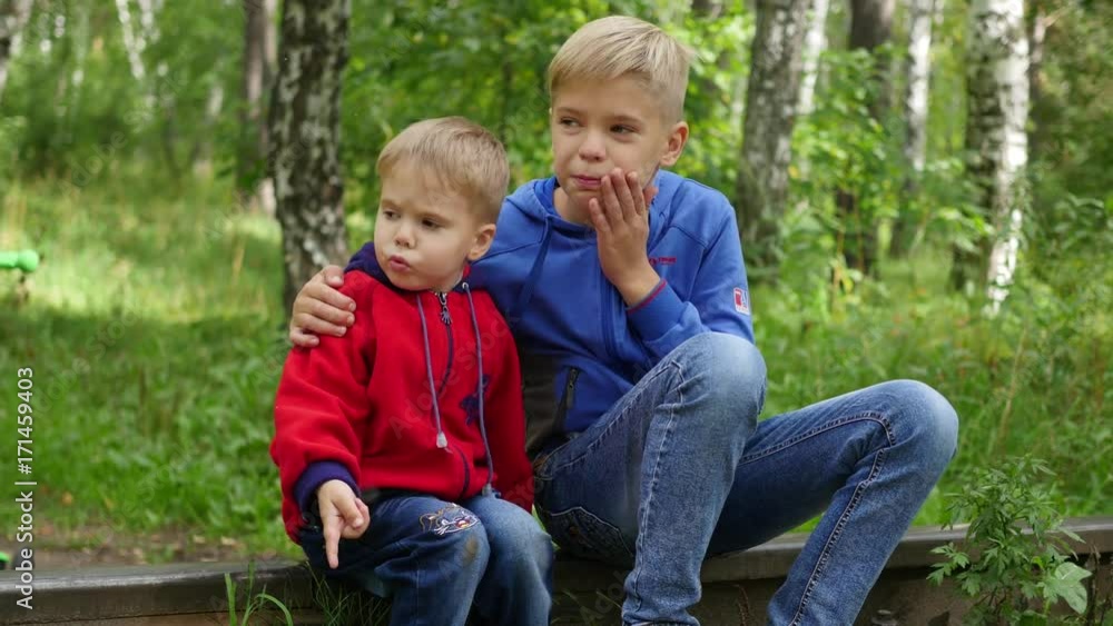 A lonely teenage boy and his younger brother sitting on the train tracks A lonely teenage boy and his younger brother sitting on the train tracks