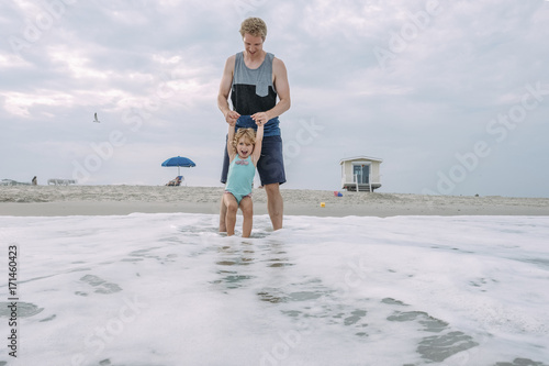 Father and daughter playing in waves at Cape May Beach against sky
