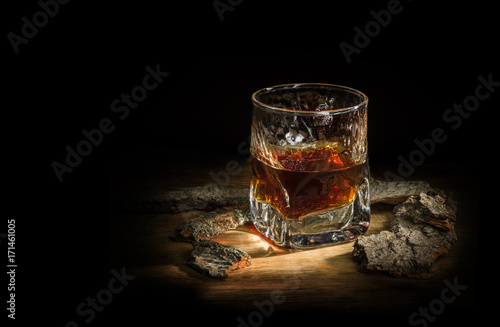 Canvas Print malt whiskey in a glass stands on a wooden board around oak chips