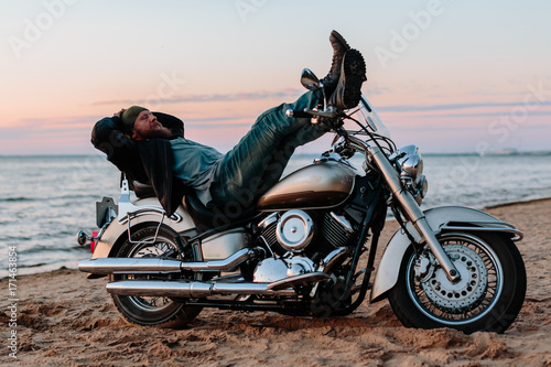 Man sleeping on a motorcycle on the beach at sunset