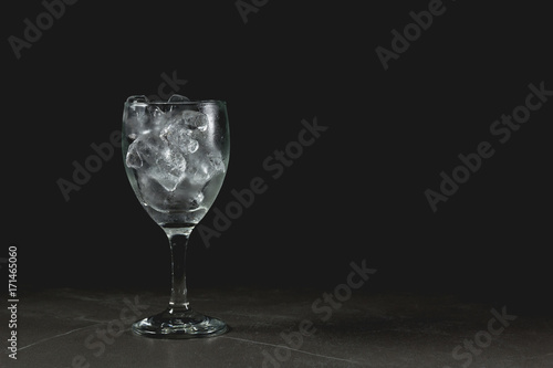 Wine glass with ice without water or wine on table, dark background.