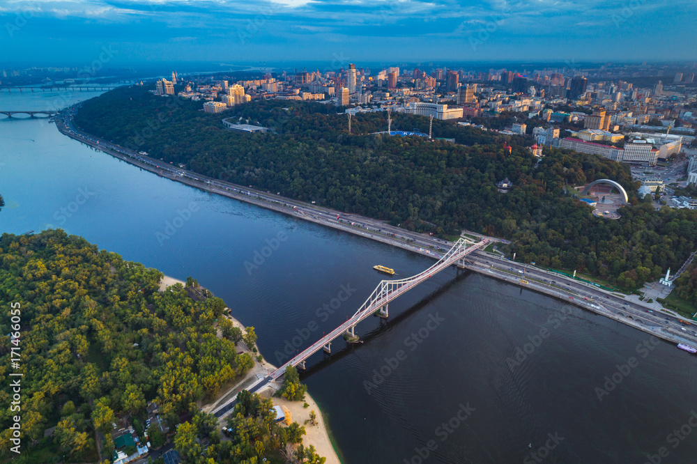 Panoramic view of the city center of Kiev. Aerial view of the right bank of Kiev with the Dnieper River, a pedestrian bridge and a large park area at sunset.
