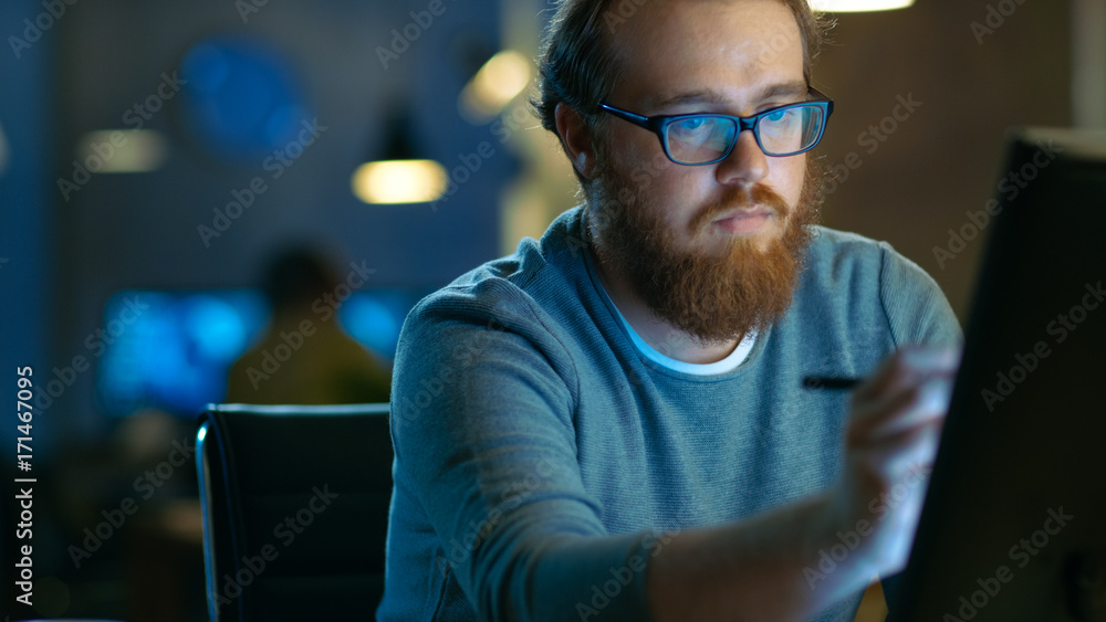 Talented Young Concept Artist Drawing on a Digital Pen Display Tablet While Sitting at His Working Place in Modern Loft Office. Late at Night. Talented Young Concept Artist Drawing on a Digital Pen Display Tablet While Sitting at His Working Place in Modern Loft Office. Late at Night.