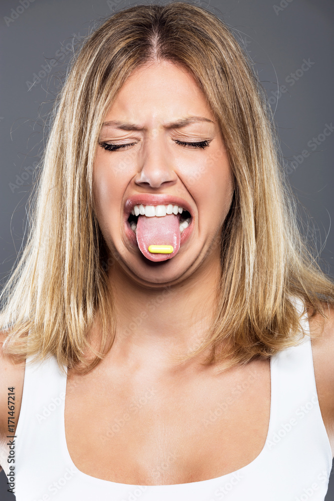 Young woman trying a pill over gray background. Young woman trying a pill over gray background.