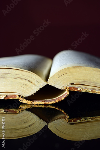 Open old thick book on black reflective table. Vertical image.