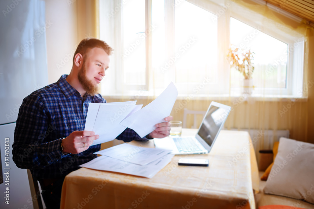 Businessman at home, he is working with a laptop, checking paperwork and bills