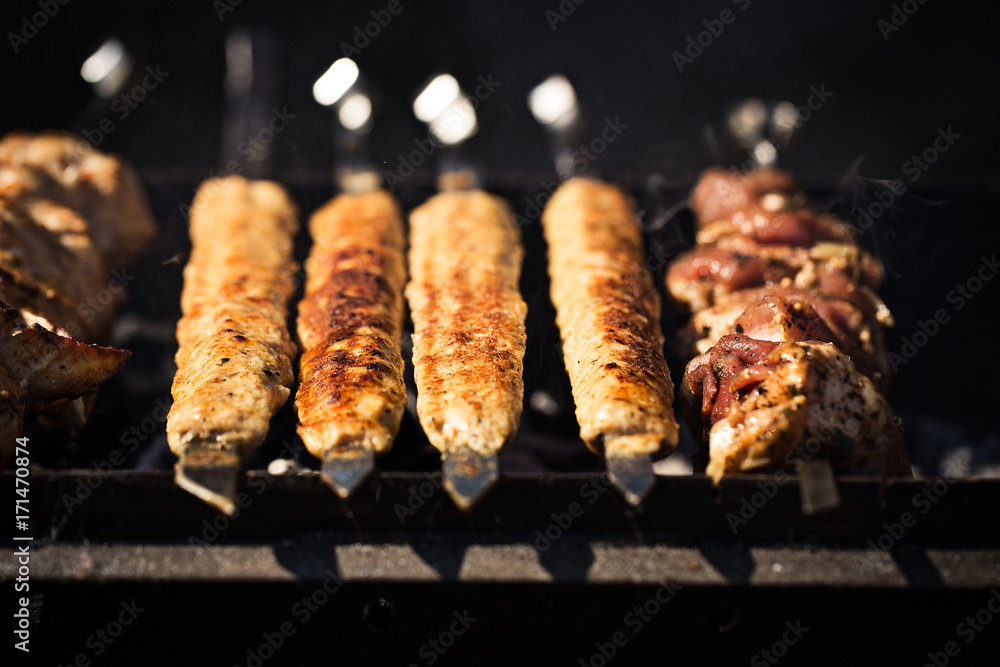 Grilled kebab cooking on metal skewer. Roasted meat cooked at barbecue.Traditional eastern dish, shish kebab. Grill on charcoal and flame, picnic Grilled kebab cooking on metal skewer. Roasted meat cooked at barbecue.Traditional eastern dish, shish kebab. Grill on charcoal and flame, picnic