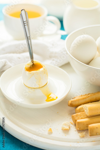 Traditional breakfast: soft-boiled eggs, green tea and bread sticks on white wooden desk. Selective focus