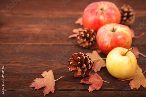 Autumn concept, fallen red-yellow currant leaves with apples and pine cones on a wooden table. Thanksgiving Day.
