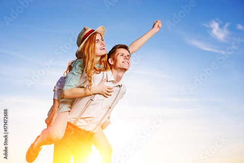 Young man piggybacking his happy girlfriend with raised hand. Cheerful lovers dreaming