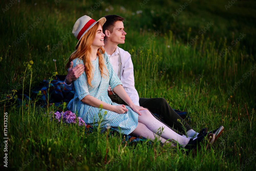 young couple sitting on the plaid in the park and look at the sunset young couple sitting on the plaid in the park and look at the sunset