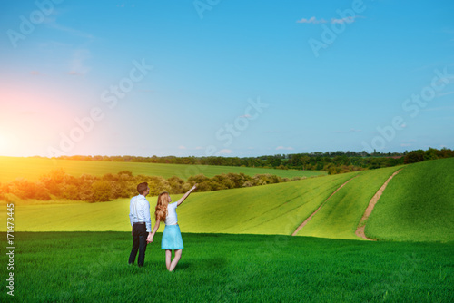 A young couple standing in the field, the girl shows her hand to the sky