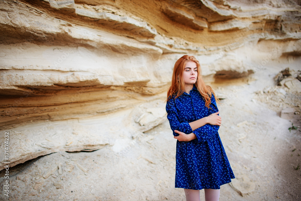 Beautiful redheaded girl standing in a blue dress in the middle of a sand quarry Beautiful redheaded girl standing in a blue dress in the middle of a sand quarry