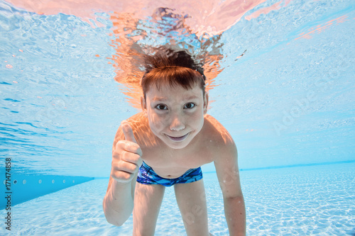 Happy young boy swim and dive underwater, kid breast stroke with fun in pool. Active healthy lifestyle, water sport activity and lessons with parents on summer family vacation with child photo