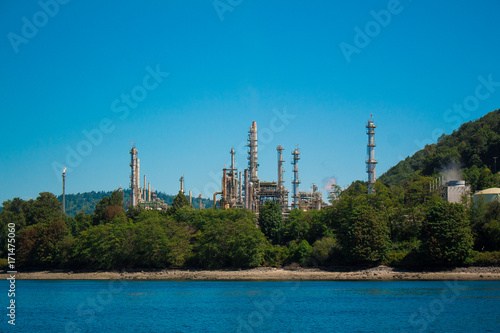 Photo of industrial site behind trees across water