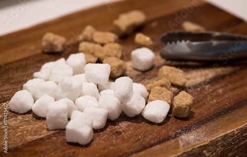 Brown cane and white sugar cubes isolated on wooden background and sugar tongs. photo