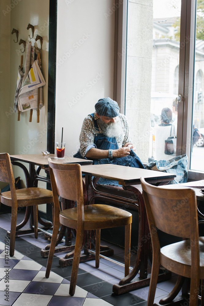 Cool Elderly Man With Long Grey Hipster Beard Sewing in Bright Restaurant Cool Elderly Man With Long Grey Hipster Beard Sewing in Bright Restaurant