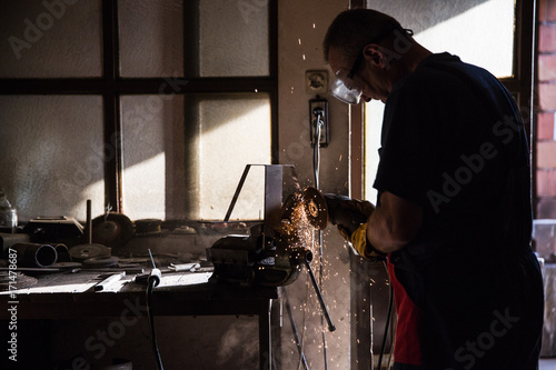 A man in a workshop using an industrial metal grinder to grind down stainless steel