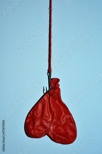 deflated heart-shapped balloon hanging from a hook upside down on a blue wall