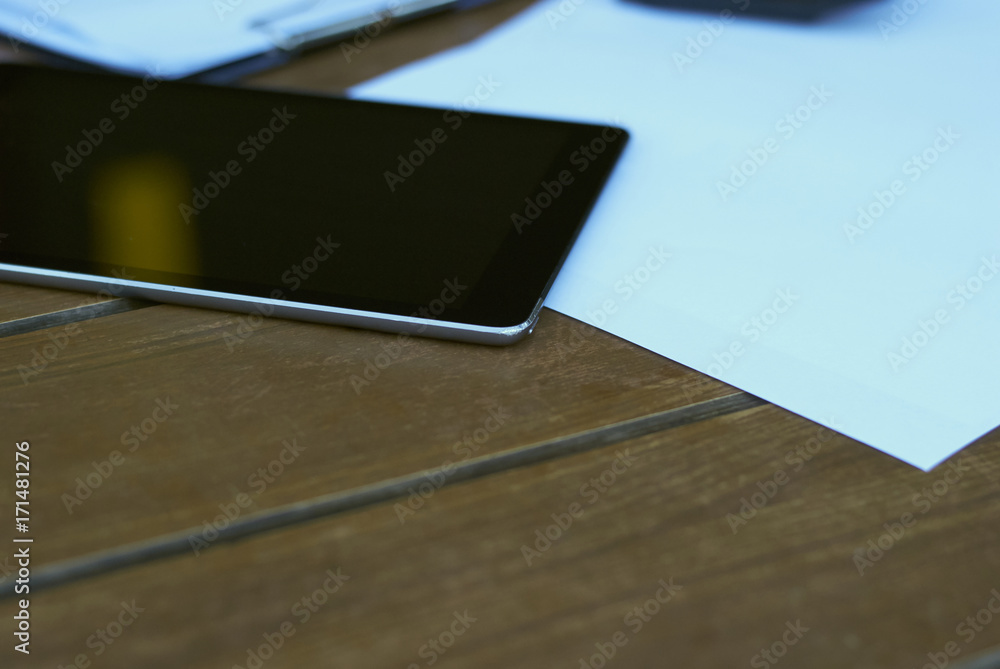 close-up a dark tablet lies on a light wooden table next to sheets of paper and a clipboard. background blur close-up a dark tablet lies on a light wooden table next to sheets of paper and a clipboard. background blur