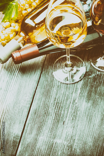 Бутылки с белым и красным вином, бокалы, виноград на деревянном столе