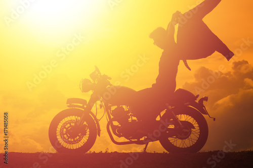 Silhouette of biker man with his motorbike beside the natural lake and beautiful  enjoying freedom and active lifestyle  having fun on a bikers tour.sunset background and sky.