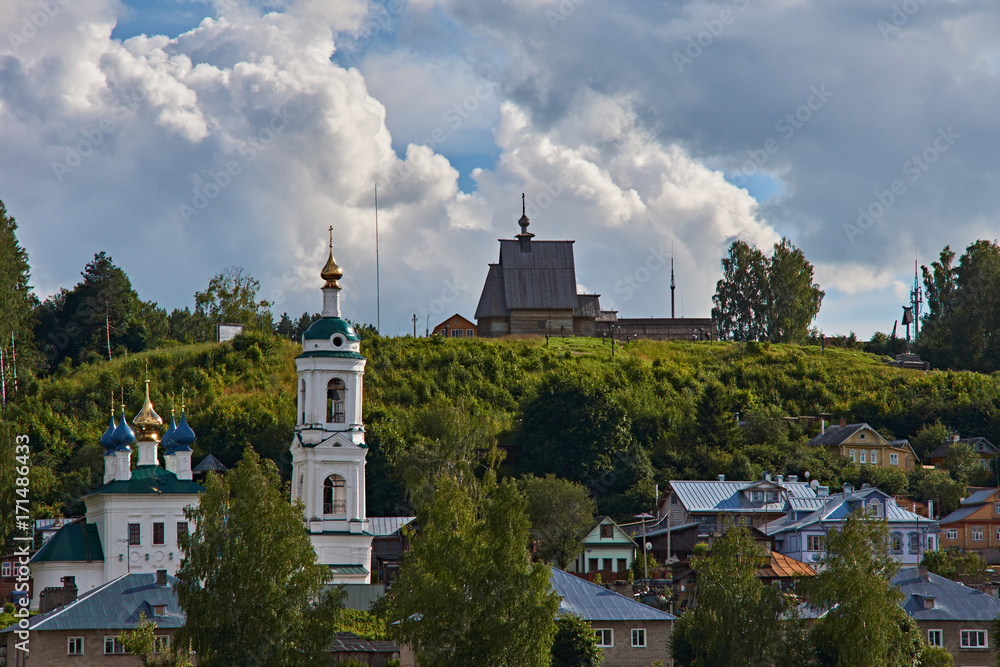 Stone and wooden temples on a hill/A white Orthodox church with a bell tower stands on a hill. Above it is a wooden one. Plyos, the Golden ring of Russia