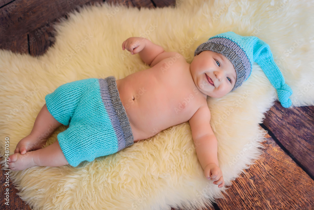 likable and pretty newborn baby boy with big blue eyes in a knitted hat on a wooden background at home