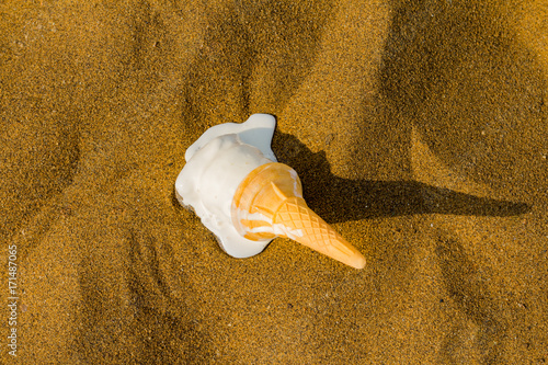 A vanilla whippy ice cream cone falls onto the sandy beach and melts in the hot summer weather. A disaster for anyone eating an ice cream. photo