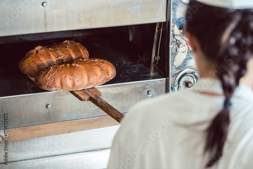 Baker woman getting fresh bread with shovel out of oven