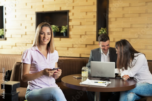 Beautiful young businesswoman is using phone while having a coffee break at coffee shop with her colleagues