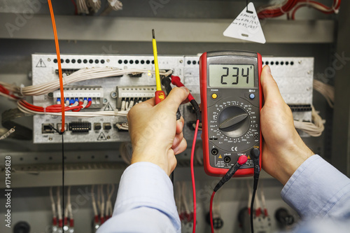 Obraz na płótnie multimeter and screwdriver in hands of electrical engineer for automation close-up. Adjustment of industrial control controller. Testing of electrical equipment. w salonie