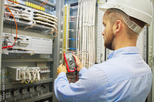 Engineer electric with multimeter. Side view of male technician examining fusebox with multimeter probe. photo