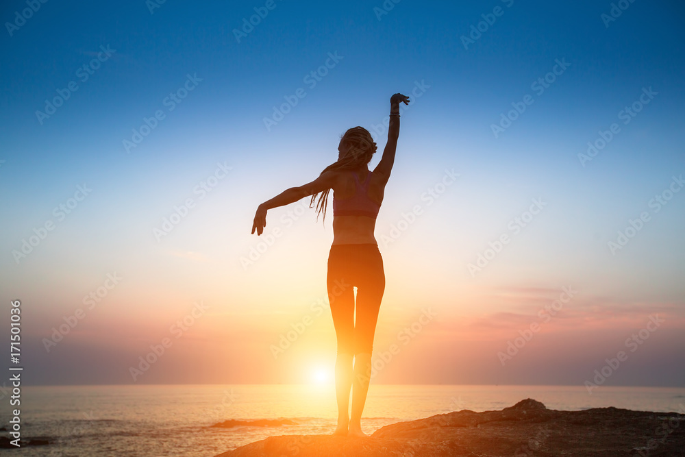 Silhouette flexible girl moves in a dance on the shore of the sea during sunrise.