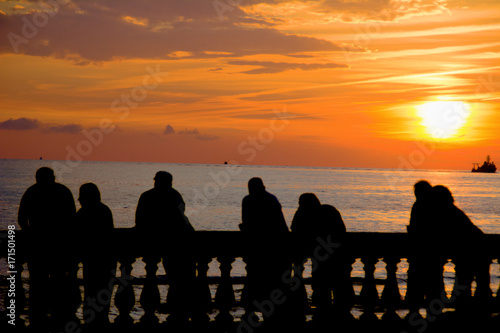 silhouette of people leaning on railing at sunset facing the sea with a submarine sailing