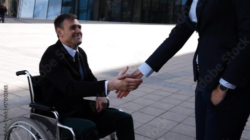 businesswoman in formal suit shaking hands with disabled colleague businessman outdoor nead cool modern business centre building at sunset. Super slow motion. High speed fps 250 cameraSunny day. photo