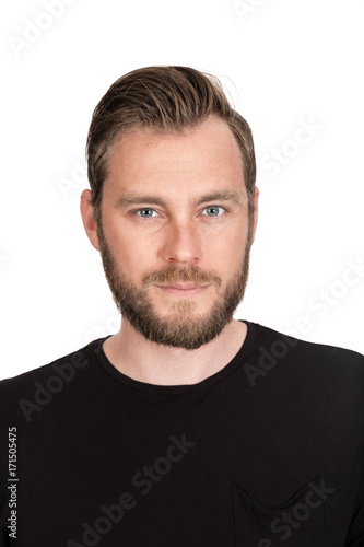Mature staring man with beard wearing a black t-shirt standing against a white background looking at camera.