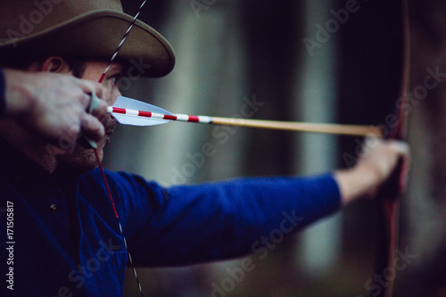Adult male archer shoots a bow and arrow in the forest at dusk photo