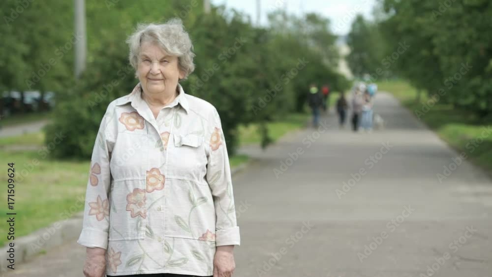 Portrait of smiling elderly woman outdoors in the background of park in summer. Slow motion Portrait of smiling elderly woman outdoors in the background of park in summer. Slow motion