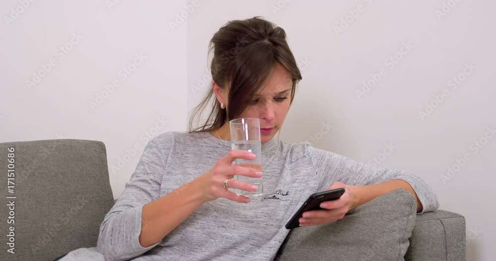 Woman on home sofa using smartphone and drinks water 4k video. Girl online in mobile phone at modern flat apartment Woman on home sofa using smartphone and drinks water 4k video. Girl online in mobile phone at modern flat apartment