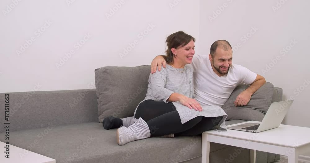 Couple at home sofa watching laptop and smiling 4k video. Happy man and woman using computer together, looking funny joke Couple at home sofa watching laptop and smiling 4k video. Happy man and woman using computer together, looking funny joke