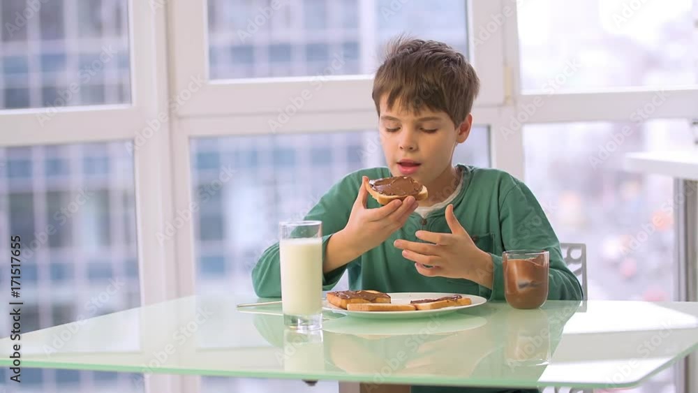 Boy child eating chocolate hazelnut spread toast HD slow-motion video. Kid morning breakfast of cocoa sweet paste on bread with milk Boy child eating chocolate hazelnut spread toast HD slow-motion video. Kid morning breakfast of cocoa sweet paste on bread with milk
