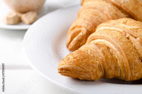 Traditional breakfast with fresh croissants and coffee on white wooden background.