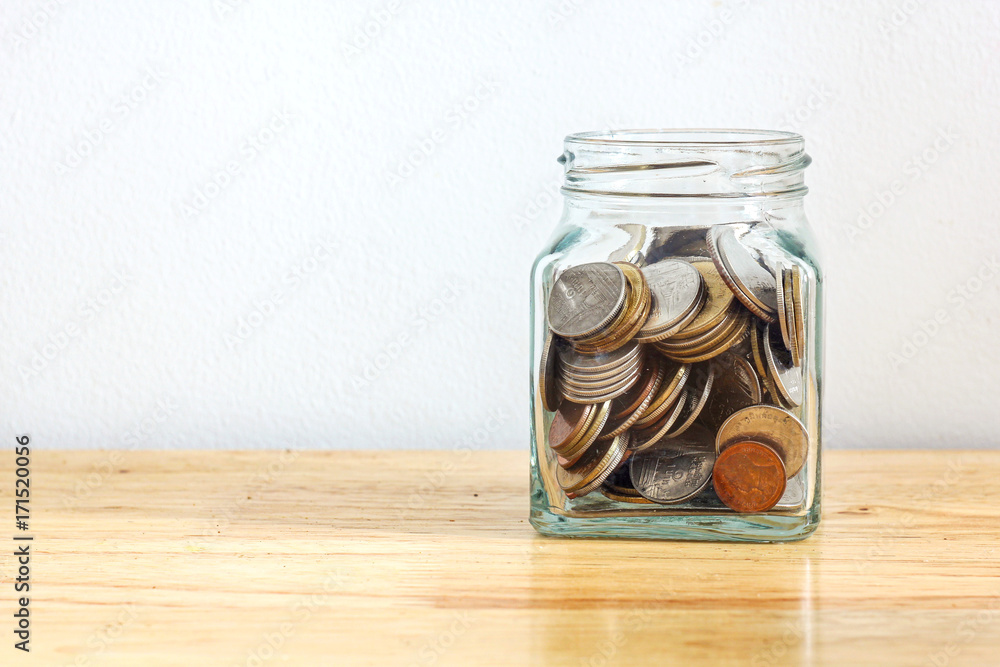 Silver and gold coin in glass jar bottle on wood table with white background Silver and gold coin in glass jar bottle on wood table with white background